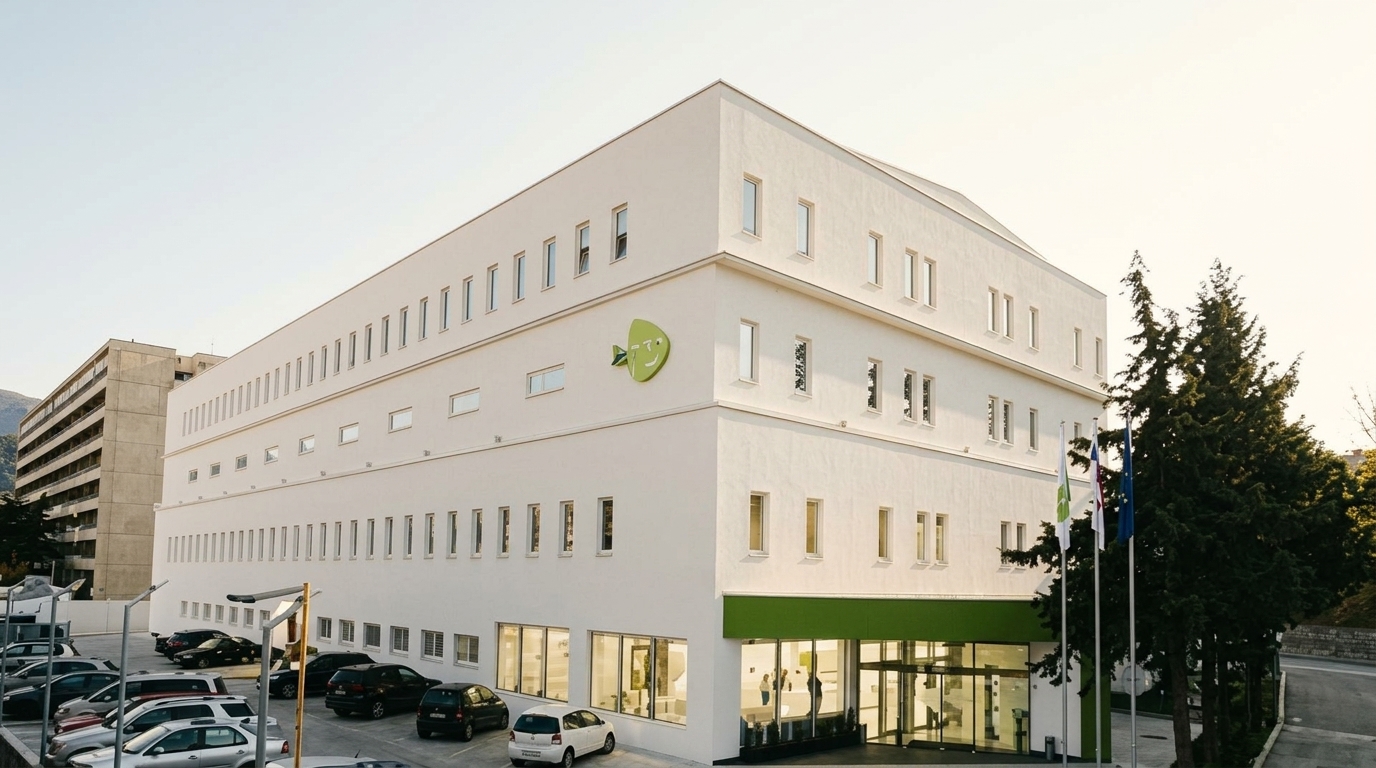 Innotech - უსაფრთხოების სისტემები White Multi-story Office Building with Green Trim and Logo on the Façade, Glass Entrance, Flagpoles, Trees, and a Parking Lot in Front