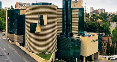Innotech Aerial View of a Modern Architectural Complex with Curved Beige Facade and Glass Towers in an Urban Setting, Beside a Tree-lined Street.