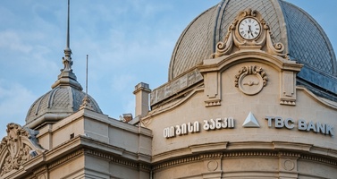 Innotech Facade of a Tbc Bank Building with a Domed Roof, Ornate Beige Stonework, a Clock, and Georgian Script on the Facade Against a Blue Sky.